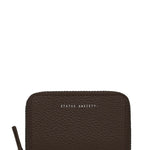 A dark brown pebbled leather zip-around wallet with 'STATUS ANXIETY' printed in white text on the front, shown on a plain white background.