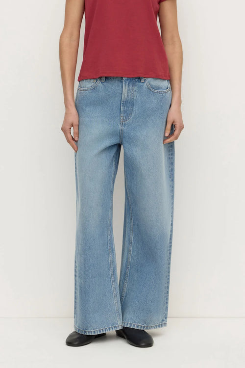 A person wearing light-wash wide-leg denim jeans with a red top and black shoes, shown from the chest down against a plain light background.