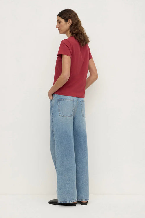 A woman shown from the back wearing a short-sleeve red t-shirt and light blue wide-leg jeans, standing against a plain white studio background.