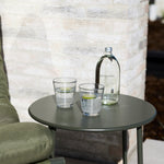 Two clear handmade bubble glass tumblers styled on a sage green outdoor side table.