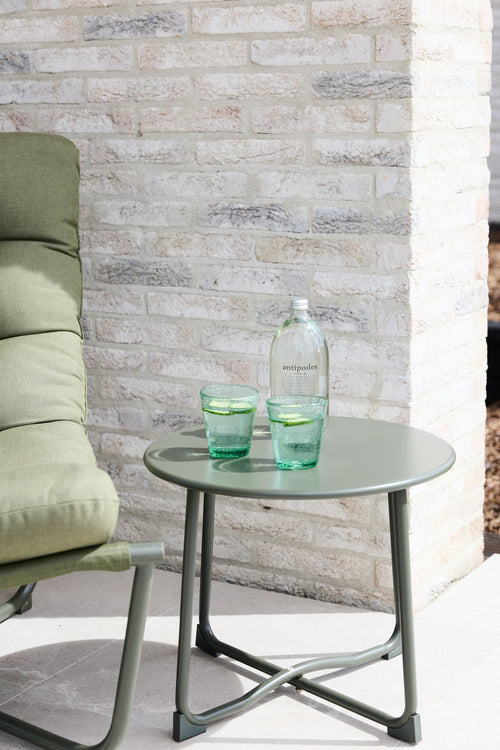 Two green handmade bubble glass tumblers styled on a sage green side table in an outdoor setting.