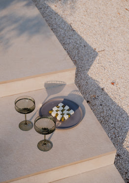Two dark green cocktail glasses on a textured surface with a blurred background