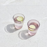 Two pink handmade bubble glass tumblers styled on a light stone surface with lime garnish.