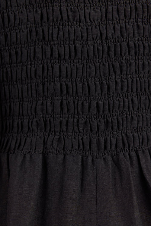 Close-up of a black smocked fabric garment, showing horizontal gathered stitching and a slightly textured material.