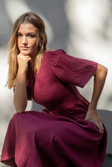 Woman in a burgundy dress sitting on the ground with a blurred background
