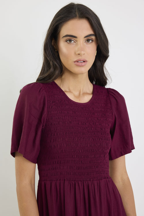 Woman wearing a burgundy dress with puff sleeves against a white background