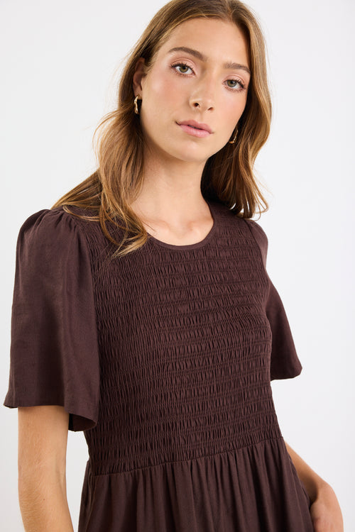 Woman wearing a brown smocked dress against a white background