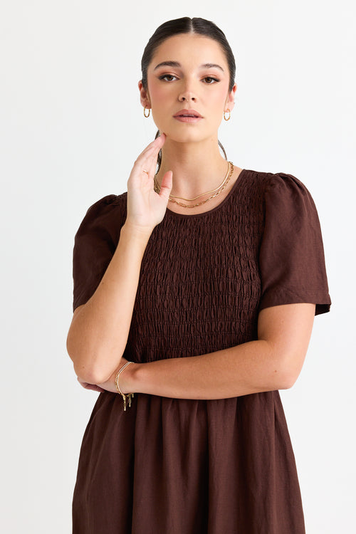 model wears a long brown linen dress with white sneakers