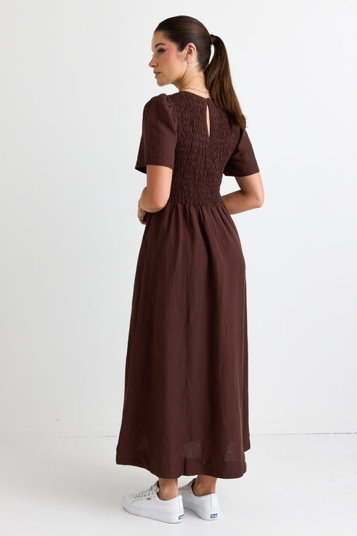 model wears a long brown linen dress with white sneakers