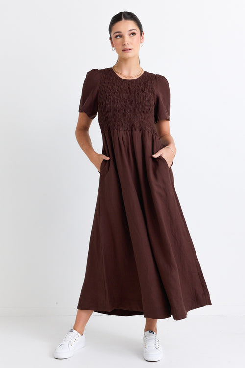 model wears a long brown linen dress with white sneakers