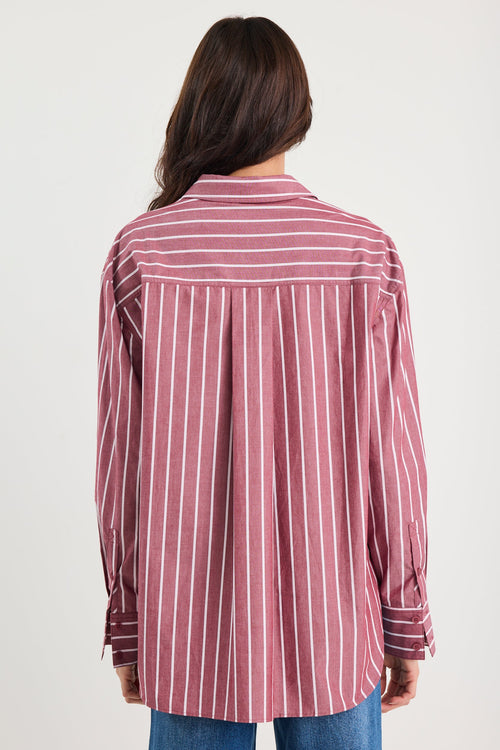 Woman wearing an oversized burgundy and white vertical stripe button-up shirt made from 100% cotton, styled with blue jeans.