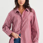 Woman wearing an oversized burgundy and white vertical stripe button-up shirt made from 100% cotton, styled with blue jeans.