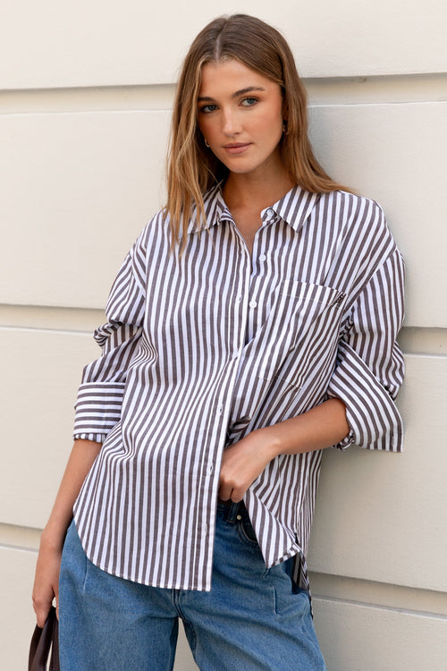 Woman wearing a striped shirt and blue jeans against a light-colored wall.