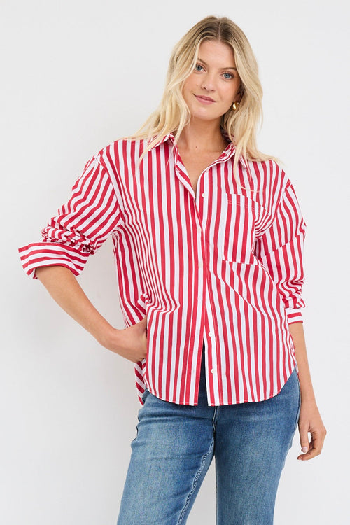 Woman wearing a red and white vertical stripe oversized button-up shirt with rolled sleeves, styled with blue jeans and loose blonde hair.