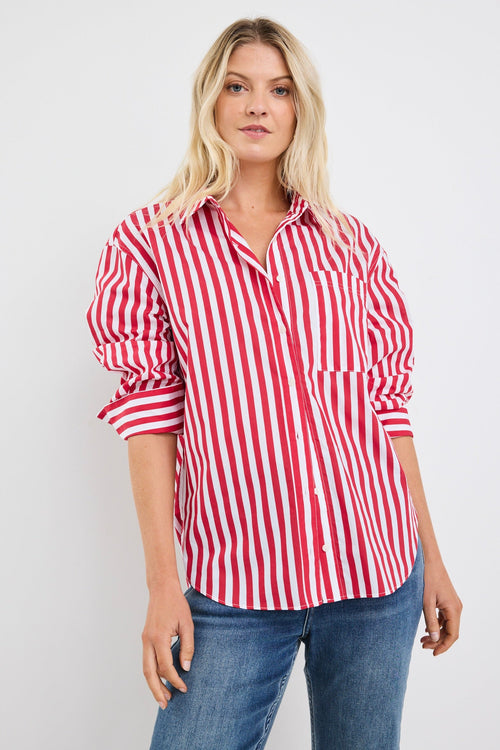 Woman wearing a red and white vertical stripe oversized button-up shirt with rolled sleeves, styled with blue jeans and loose blonde hair.
