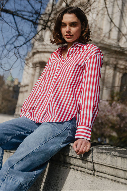 Woman in a red and white striped shirt and blue jeans sitting in front of a cathedral.