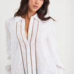 Woman wearing a white blouse with decorative stitching on a plain background