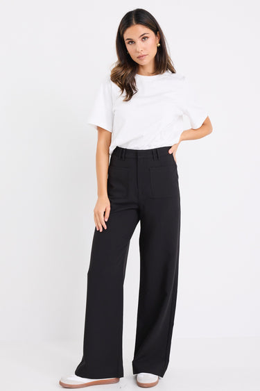 woman wearing high-waisted black wide-leg pants with front patch pockets, styled with a white tee and white sneakers.