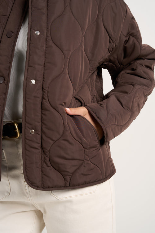 model wears a chocolate brown collarless puffer jacket with  cream jeans