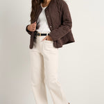 model wears a chocolate brown collarless puffer jacket with  cream jeans