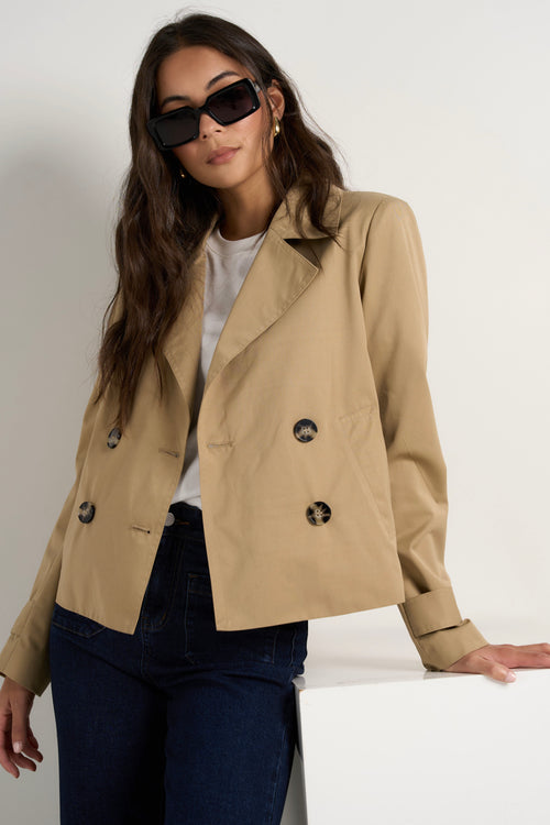 Model wears camel beige trench coat with dark indigo jeans