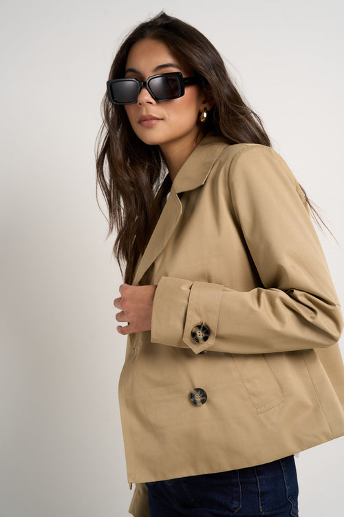 Model wears camel beige trench coat with dark indigo jeans