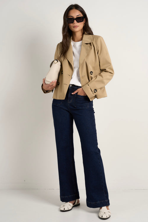 Model wears camel beige trench coat with dark indigo jeans