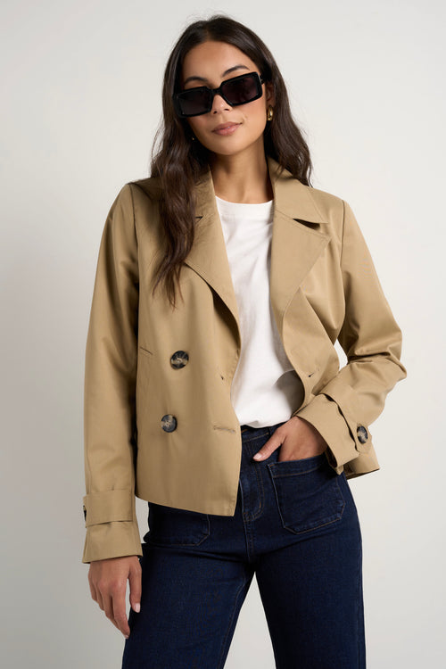 Model wears camel beige trench coat with dark indigo jeans