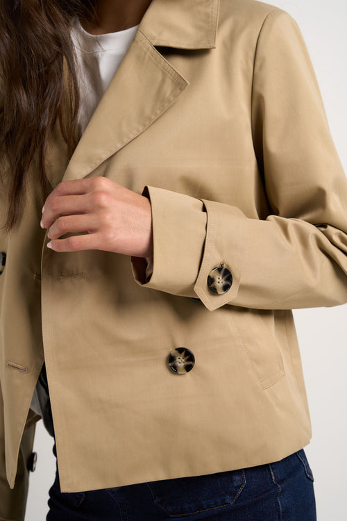 Model wears camel beige trench coat with dark indigo jeans