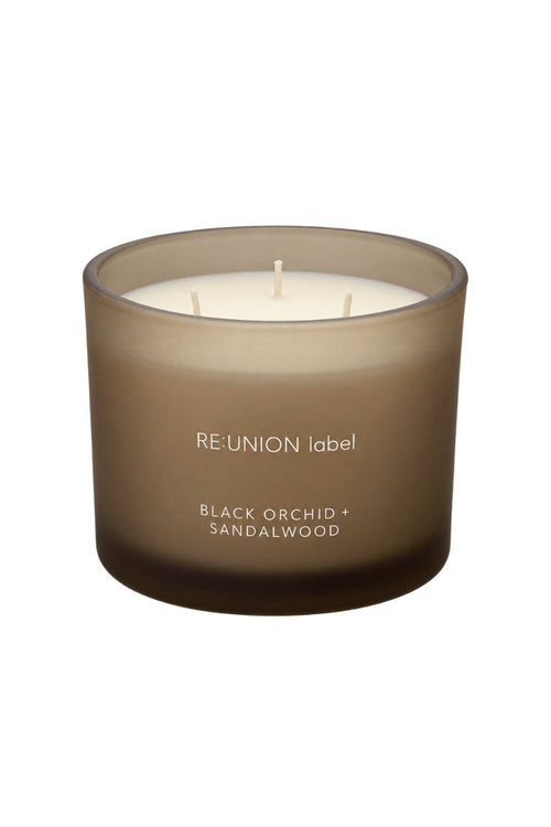 A single-reed scented candle in a frosted, translucent taupe-brown glass jar with white wax. The label reads 'RE:UNION label' and 'BLACK ORCHID + SANDALWOOD'.