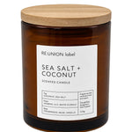 A 210g scented candle in an amber glass jar with a light wood lid, featuring a white label that reads 'RE-UNION label SEA SALT + COCONUT'.