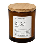 A Re:Union Label Sea Salt + Coconut scented candle in an amber glass jar with a light wood lid, shown on a plain white background.