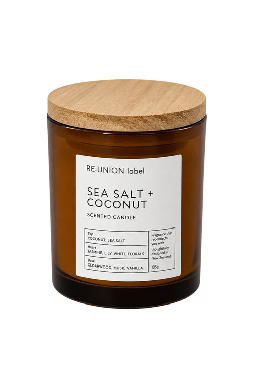 A Re:Union Label Sea Salt + Coconut scented candle in an amber glass jar with a light wood lid, shown on a plain white background.