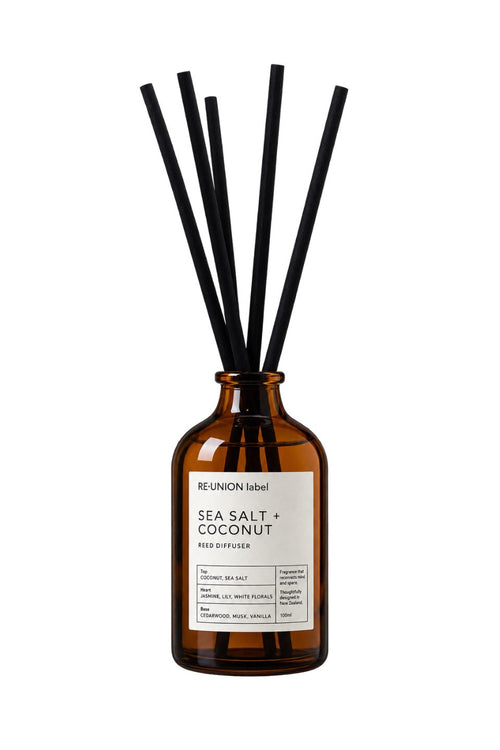 Amber glass reed diffuser bottle with a white label reading 'RE:UNION label SEA SALT + COCONUT' and six black reed straws, shown on a plain white background.