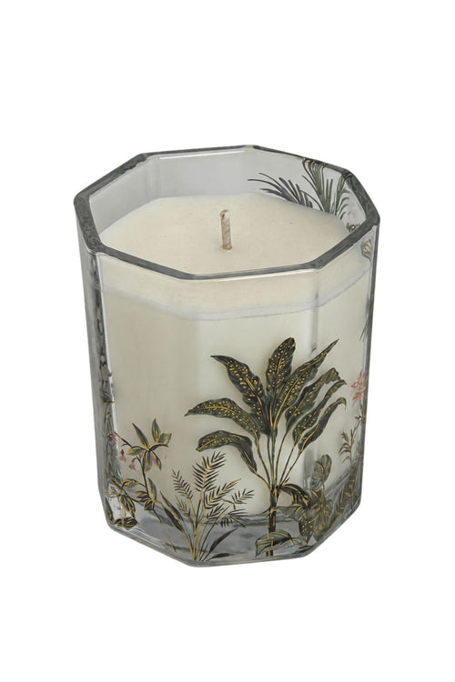 A white wax candle in a clear octagonal glass container decorated with a botanical pattern of green and gold tropical leaves, shown on a white background.