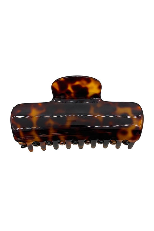 A classic hair claw clip in a glossy tortoiseshell pattern, featuring dark brown and amber-orange mottled tones with white contrast stitching, shown against a plain white background.