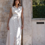 Woman in a white dress standing against a textured wall with greenery in the background