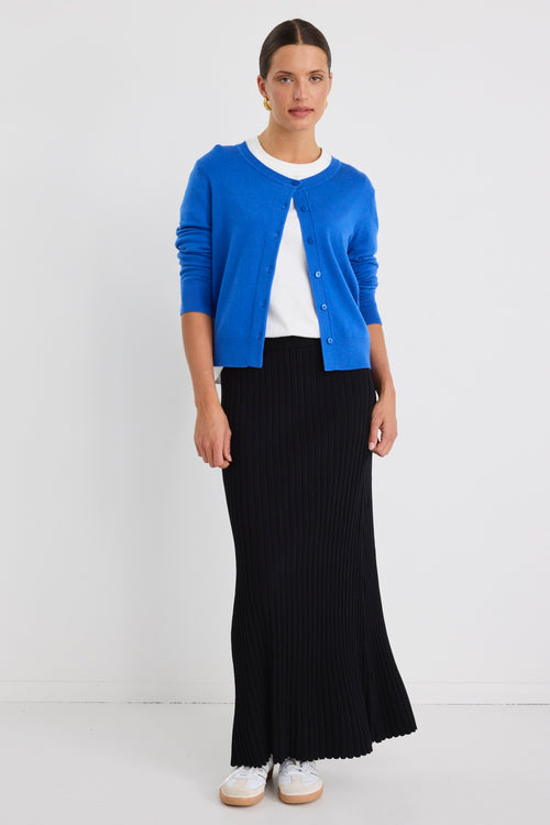 Woman wearing a white boxy tee tucked into a full-length black rib knit skirt with flared hem, styled with white sneakers.