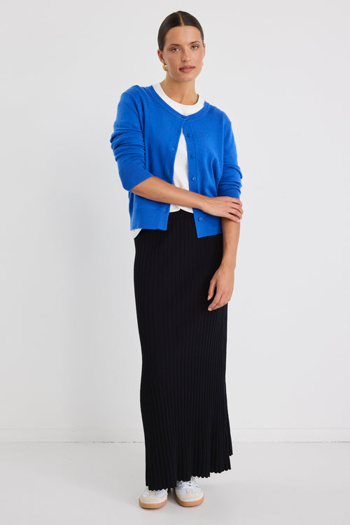 Woman wearing a white boxy tee tucked into a full-length black rib knit skirt with flared hem, styled with white sneakers.