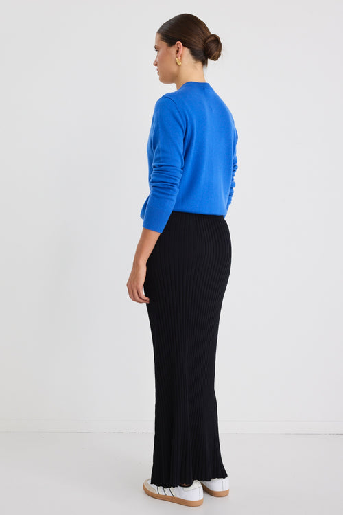 Woman wearing a white boxy tee tucked into a full-length black rib knit skirt with flared hem, styled with white sneakers.