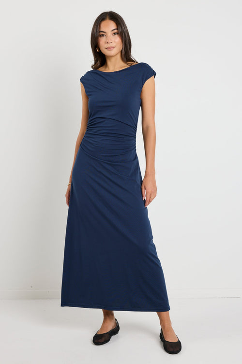 Woman wearing a navy maxi dress styled as a cowl neck and one-shoulder look, highlighting its versatile design and elegant ruched detailing.