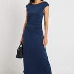 Woman wearing a navy maxi dress styled as a cowl neck and one-shoulder look, highlighting its versatile design and elegant ruched detailing.