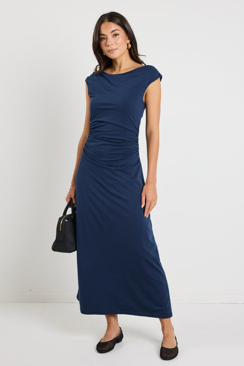 Woman wearing a navy maxi dress styled as a cowl neck and one-shoulder look, highlighting its versatile design and elegant ruched detailing.