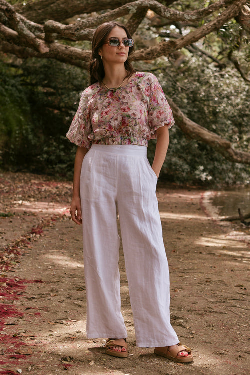 model poses on beach with floral red top and white pants