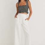 model in black floral cami top and white pants with black slides