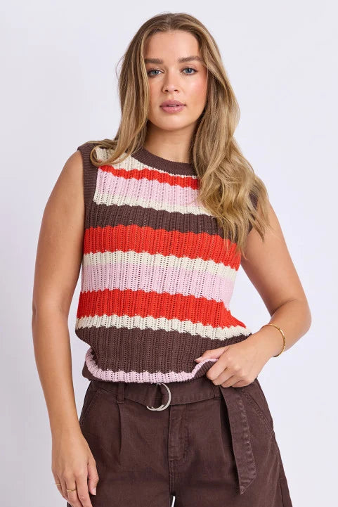 A woman modeling a sleeveless ribbed knit top with horizontal stripes in brown, red, orange, cream, and light pink, paired with brown shorts against a light gray studio background.