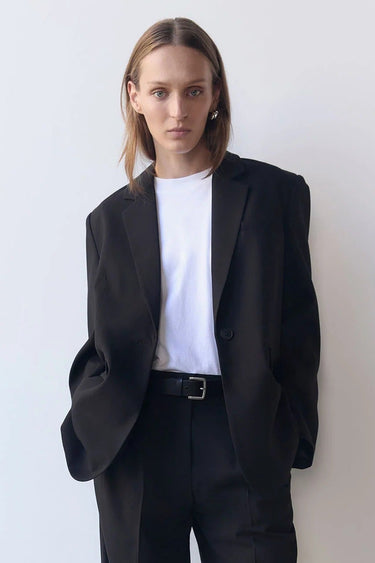Person wearing a black suit and white shirt against a plain background