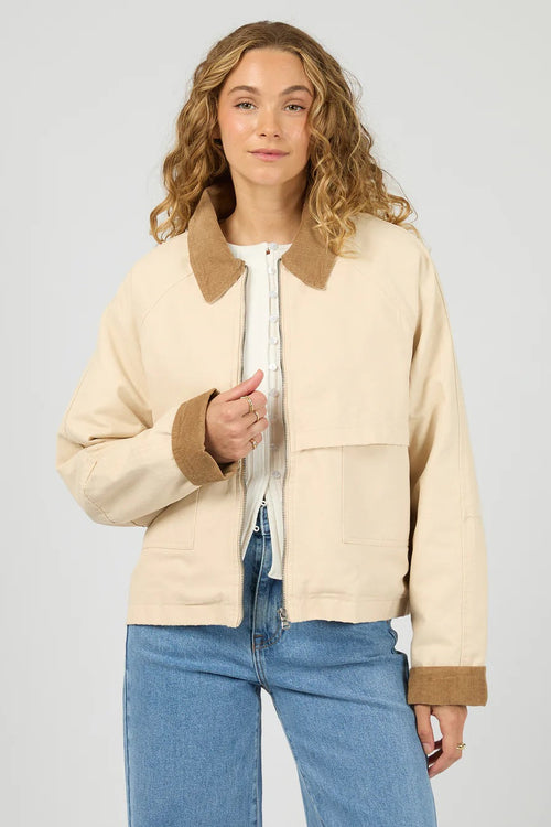 Woman wearing a beige jacket with brown collar and cuffs on a plain background