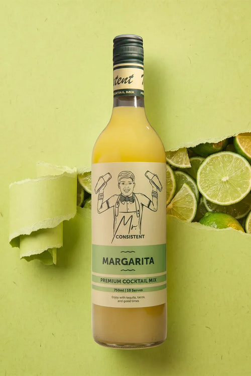 A bottle of Consistent Margarita premium cocktail mix stands upright on a light green background with torn-paper effects and lime slices around it. The bottle contains a pale yellow-orange liquid and has a cream label with a black line drawing of a bartender and green text.