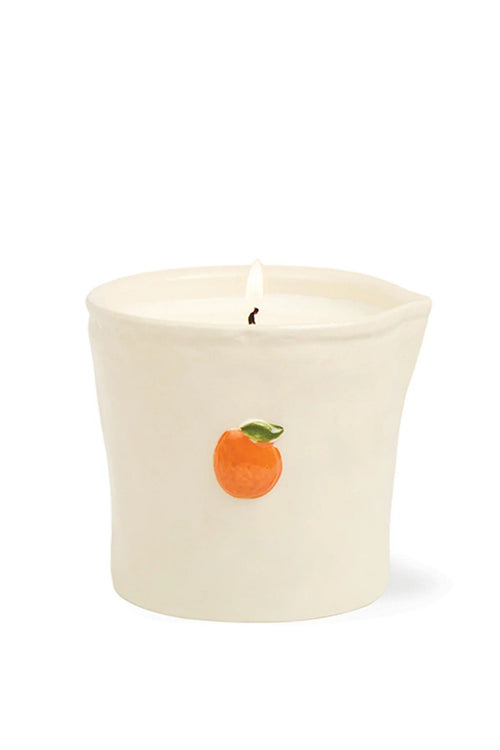 A lit cream-colored ceramic candle holder with a small orange and green leaf illustration on the front, set against a plain white background.